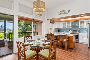 A spacious kitchen with a dining area, large windows, and a view of greenery. - Ocean-view 1BR Kapalua condo with balcony, pool, AC, and full kitchen-Kapalua Ridge Villas 2521 (Lahaina)
