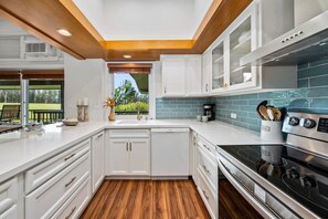A modern kitchen with white cabinetry, a stainless steel stove, and a view of the outdoors. - Ocean-view 1BR Kapalua condo with balcony, pool, AC, and full kitchen-Kapalua Ridge Villas 2521 (Lahaina)