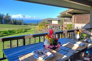 A dining table with a view of the ocean, a flower arrangement, and a glass of drink. - Ocean-view 1BR Kapalua condo with balcony, pool, AC, and full kitchen-Kapalua Ridge Villas 2521 (Lahaina)
