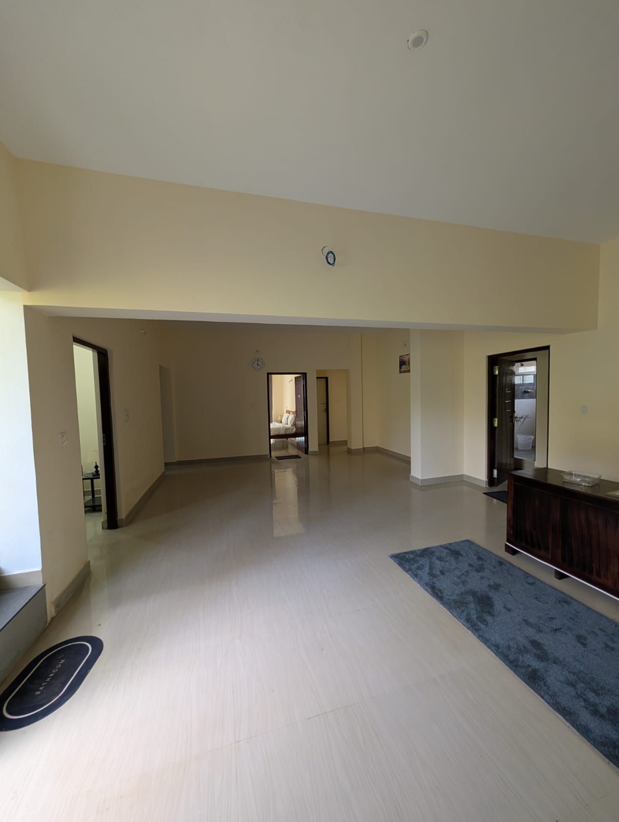 Un amplio espacio de estar con piso de color claro, alfombra azul oscuro y un mueble de madera.