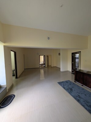 A spacious living area with a light-colored floor, a dark blue rug, and a wooden cabinet.