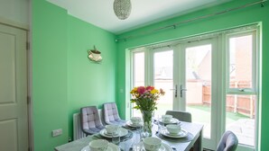 A dining area with a table set for four, chairs, a vase with flowers, and a view of the outside. - Einstein House: Spacious home for Contractors, Groups & Families (Northampton)