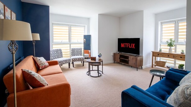 A living room with a sofa, armchair, TV, and a small table. - Einstein House: Spacious home for Contractors, Groups & Families (Northampton)