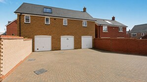 A two-story brick house with three garage doors, a paved driveway, and a clear blue sky. - Einstein House: Spacious home for Contractors, Groups & Families (Northampton)