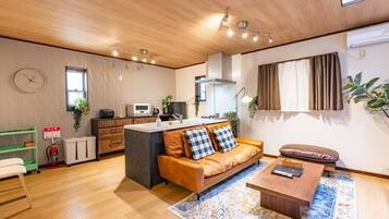 A modern living space with a wooden ceiling, a sofa with checkered cushions, a coffee table, and a kitchen area with a microwave.