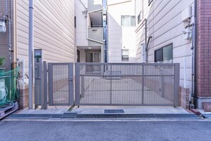 A gated entrance to a residential building with a metal gate, a narrow alleyway, and a building with a visible door and windows. - NIKYO Senzo Villa Private Villa OSAKA (Osaka)