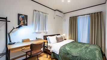 A hotel room with a bed, desk, chair, and a painting on the wall.