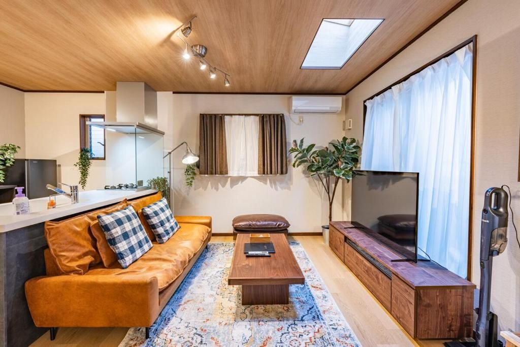 A modern living room with a sofa, coffee table, TV, and a kitchen area with a refrigerator and sink.