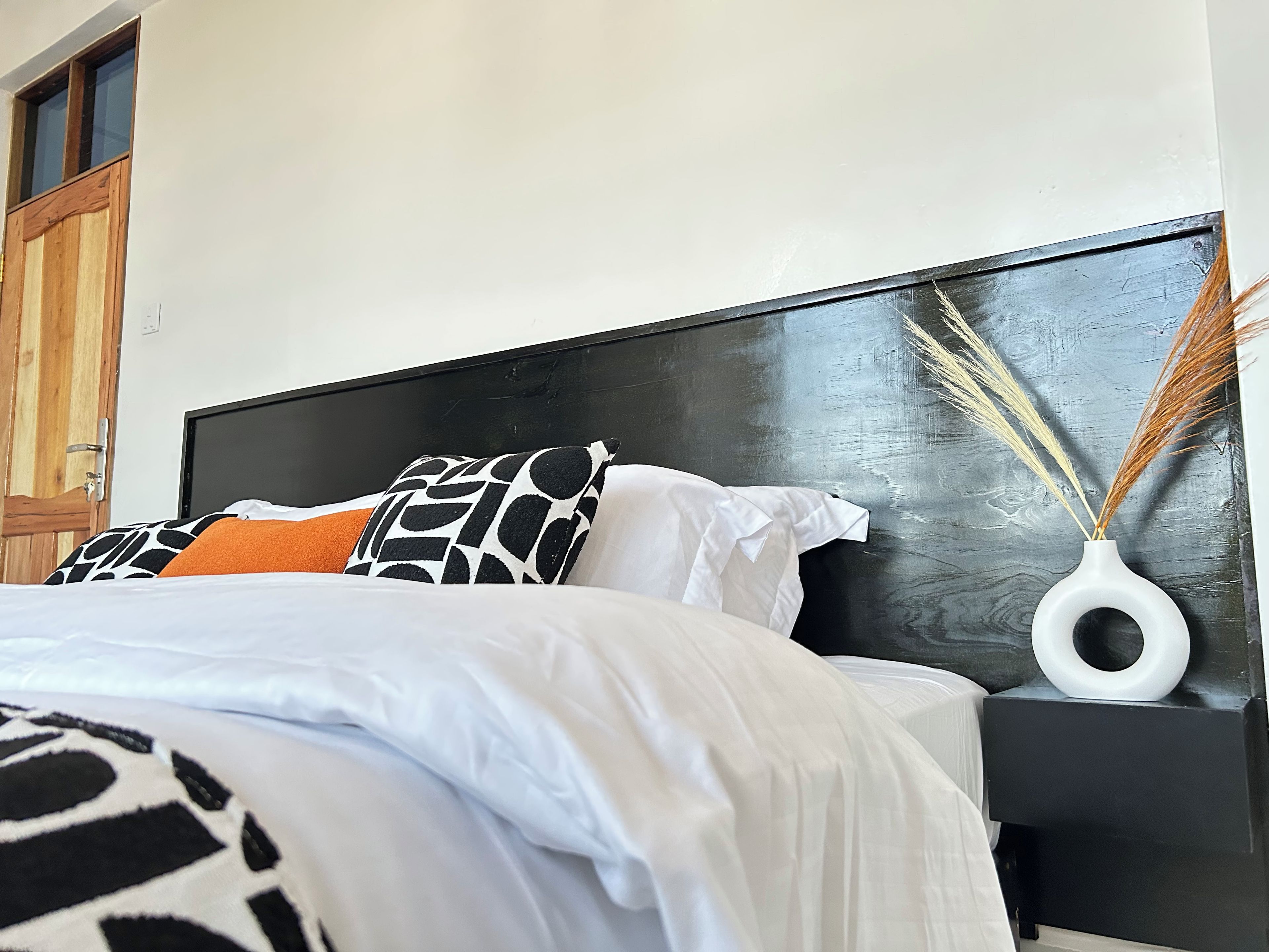A bed with a black headboard, white bedding, and patterned pillows.
