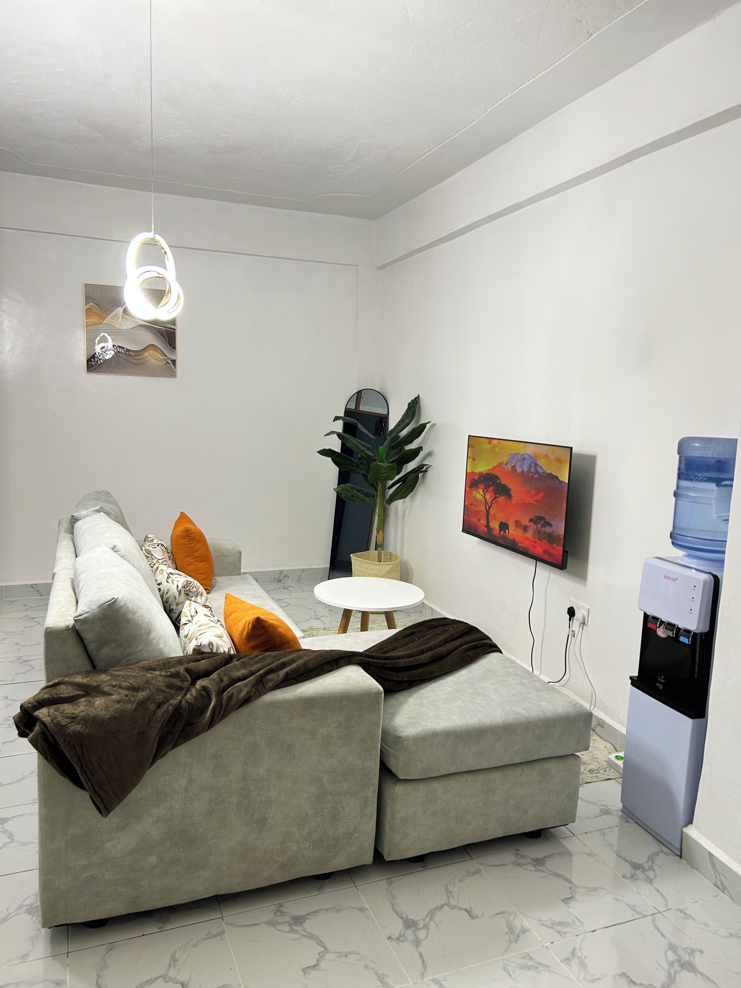 Una sala de estar moderna con un sofá seccional gris, una mesa redonda blanca y un dispensador de agua.
