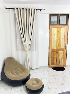 A room with a wooden door, a curtain, a beige and black bean bag chair, and a small round ottoman.