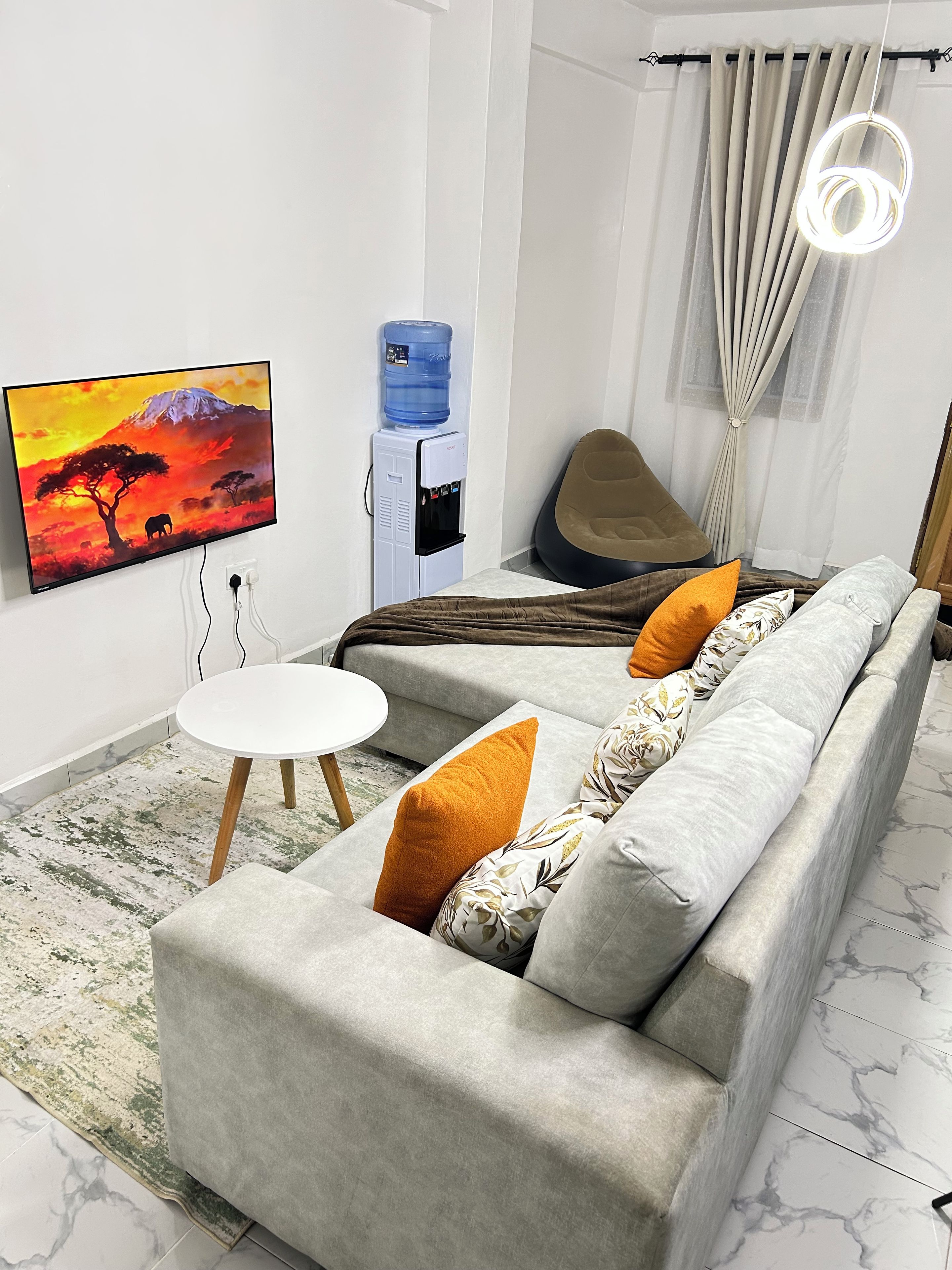 Ein modernes Wohnzimmer mit einer Couch, einem Couchtisch, einem Flachbildfernseher, einem Wasserspender und einem Vorhang.