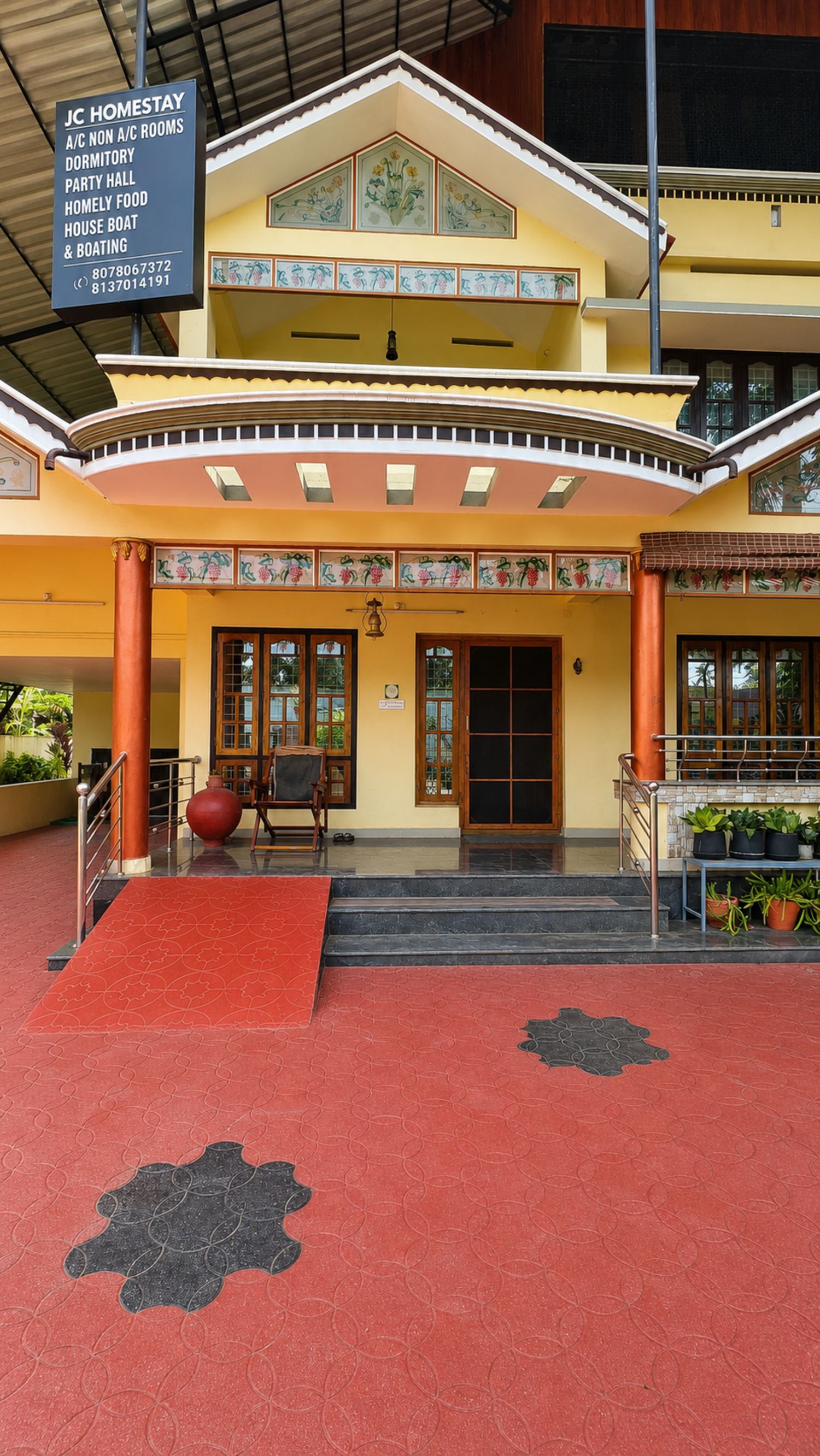 A two-story building with a red carpeted entrance, a signboard with amenities, and a traditional architectural style.