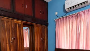 A bedroom with a bed, wooden wardrobe, and an air conditioning unit.