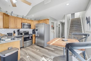 A modern kitchen with wooden cabinets, stainless steel appliances, a granite countertop, and a herringbone-patterned floor. - Derby House (Louisville)