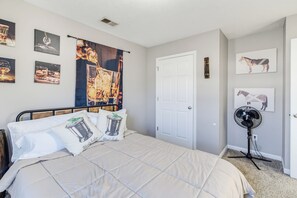 Quarto com cama, almofadas, ventoinha na parede e diversos quadros emoldurados.