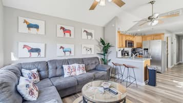 Een moderne woonkamer met een grijze bank, een glazen salontafel en muurdecoratie met paarden.