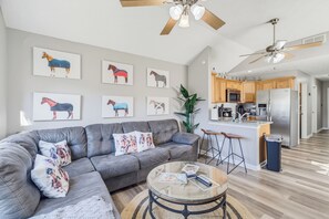 Uma sala de estar moderna com um sofá cinzento, uma mesa de centro de vidro e quadros de cavalos na parede.