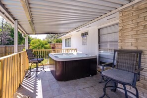 Eine überdachte Terrasse mit Whirlpool, zwei Stühlen und einem Holzzaun.