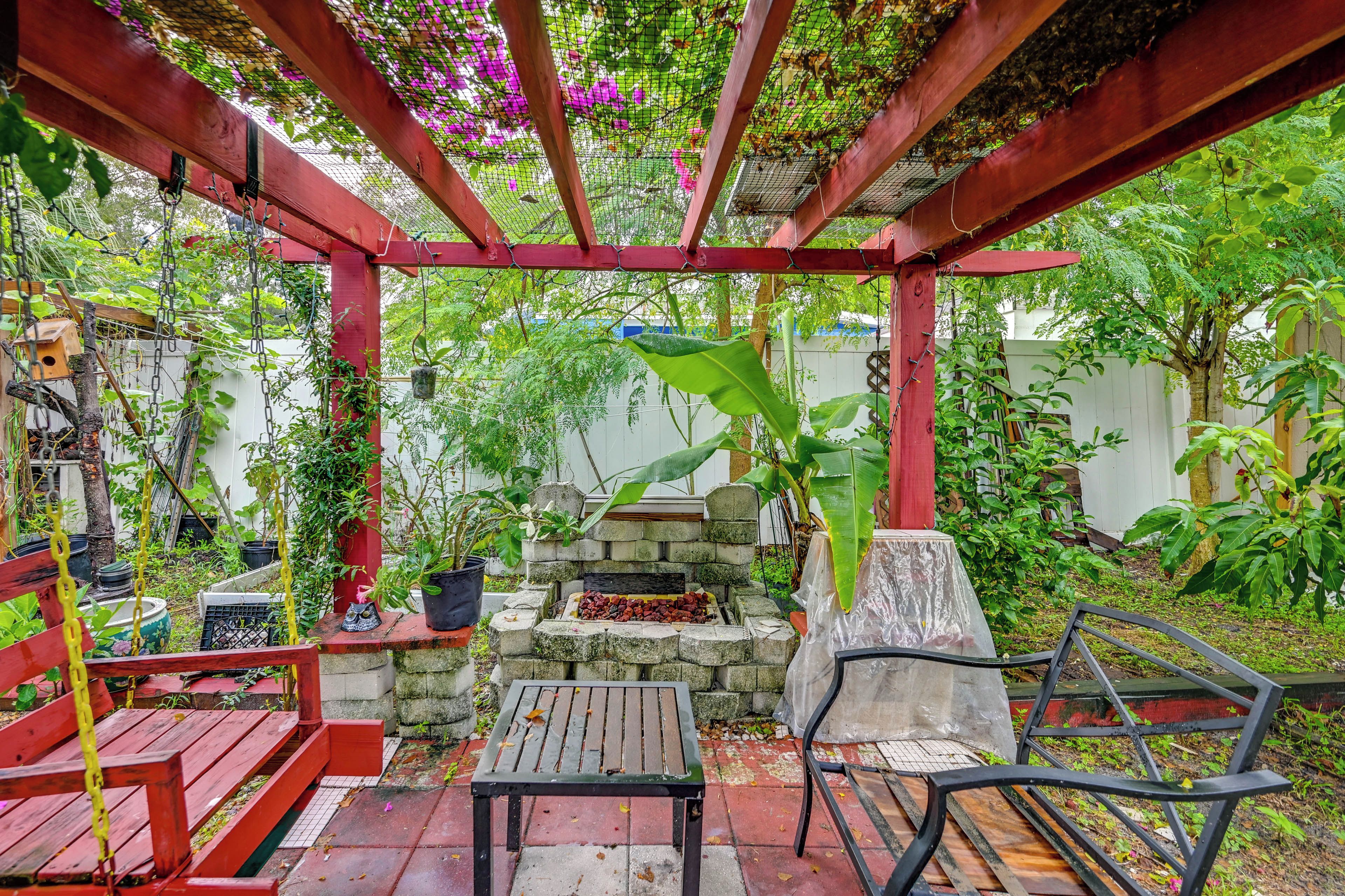A covered outdoor seating area with a stone fire feature and various plants.