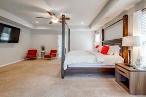 A bedroom with a large bed, a ceiling fan, a TV mounted on the wall, and a small table with a lamp. - McDonough Group Getaway: Pool, Patio + Game Room (McDonough)