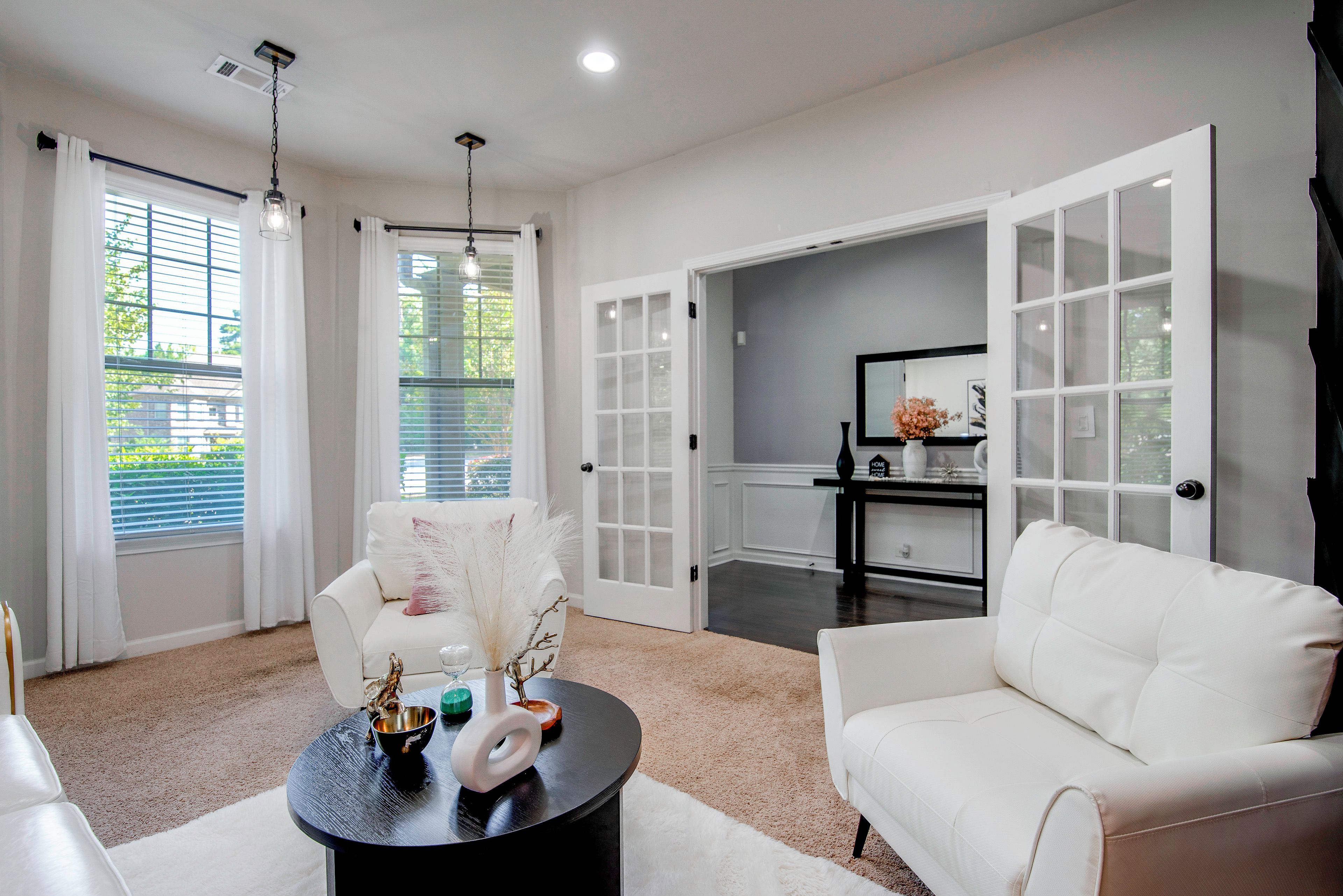 A modern living room with a white sofa, a round coffee table with decorative items, and a view through a glass door.