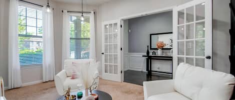 Una sala de estar moderna con un sofá blanco, una mesa redonda de centro con objetos decorativos, y vistas a través de un ventanal.