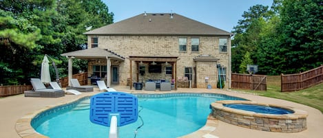 Un jardin avec une piscine, un jacuzzi et un espace patio couvert.