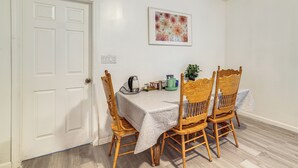 Ein Essbereich mit einem Tisch, gedeckt für vier Personen, umgeben von Holzstühlen, einem Wasserkocher und einem gerahmten Blumenbild an der Wand.