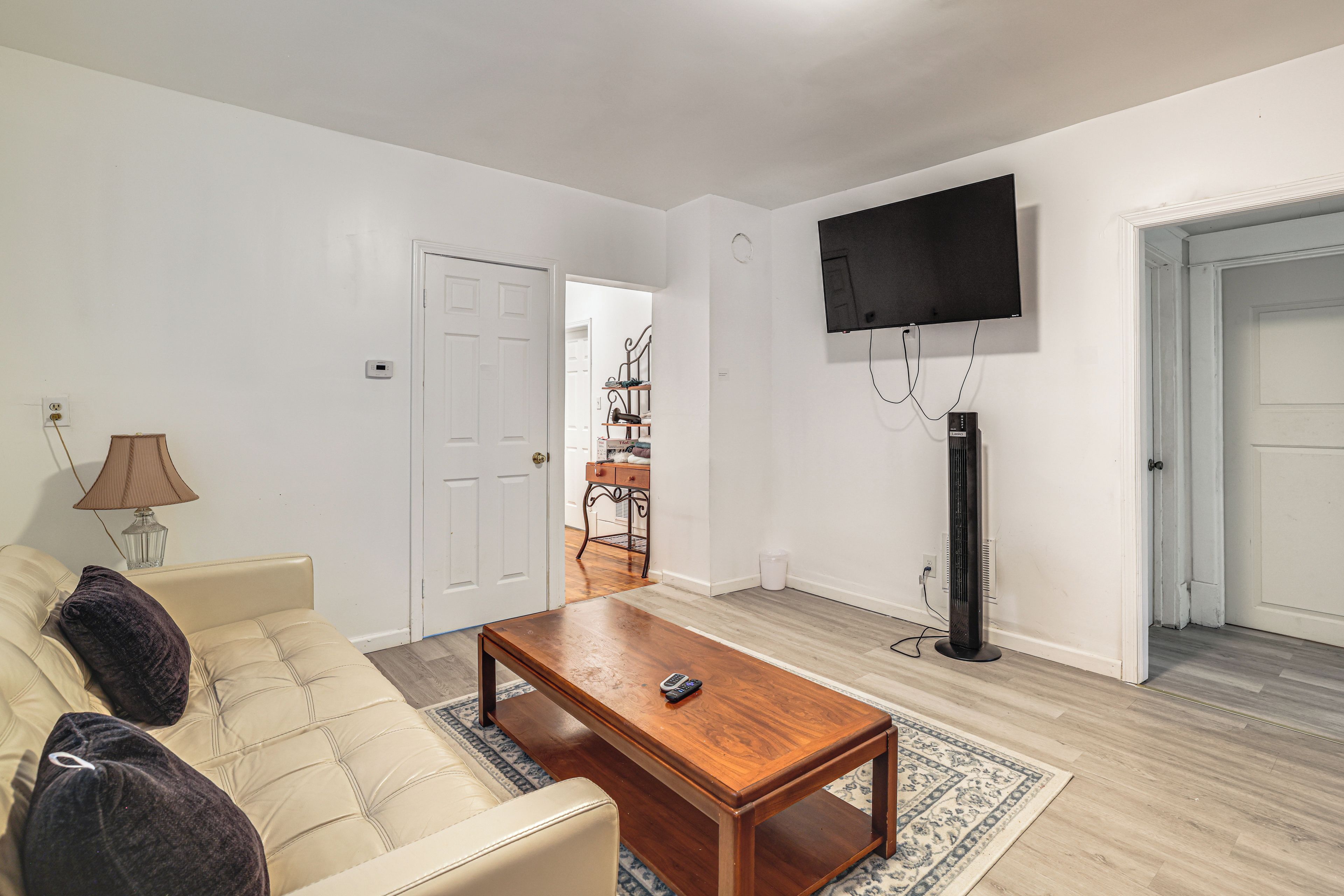 Ein Wohnzimmer mit einem beigen Sofa, einem Holztisch, einem flachbildfernseher an der Wand und einer Lampe auf einem Beistelltisch.