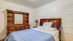 Ein Schlafzimmer mit Bett, Kommode, Spiegel und Tür.
