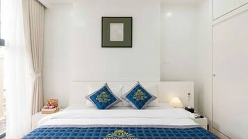 Quarto de hotel com cama, almofadas, mesa de cabeceira, luminária e quadro pendurado na parede.