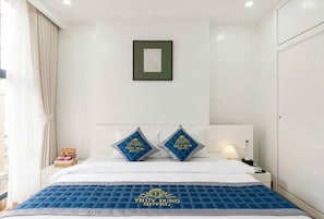 A hotel room with a bed, two pillows with the hotel's logo, a framed picture on the wall, and a nightstand with a lamp. - Thuy Dung Hotel (Tu Liem)