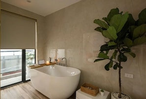 A modern bathroom with a freestanding bathtub, a large potted plant, and a view of the outdoors through a sliding door. - Thuy Dung Hotel (Tu Liem)