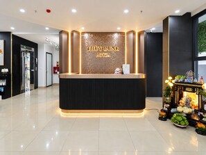 A hotel reception desk with a modern design, a digital sign displaying the hotel name, and a small shrine with offerings. - Thuy Dung Hotel (Tu Liem)