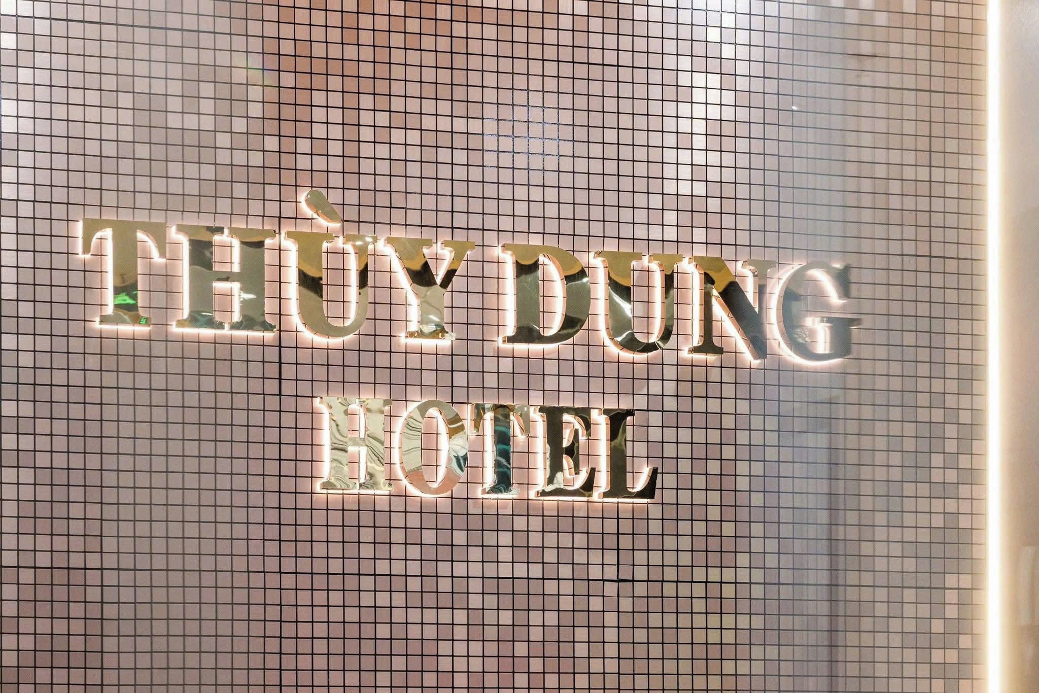 A hotel sign with illuminated letters spelling 'THUY DUNG HOTEL' against a tiled wall.
