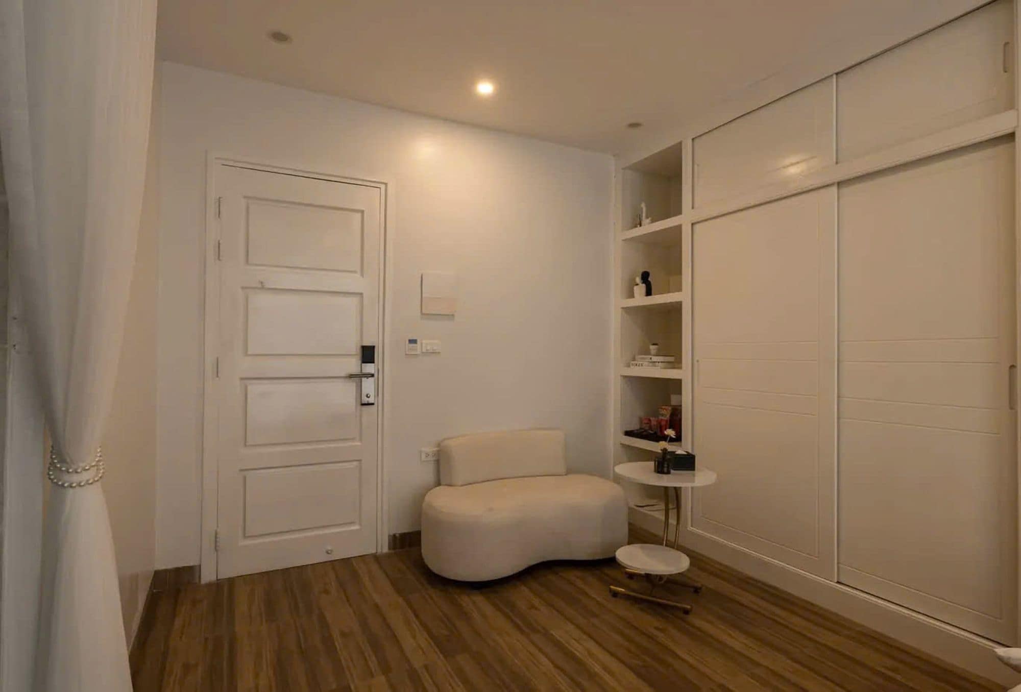 Une pièce avec une porte blanche, un canapé blanc, une petite table ronde et des étagères intégrées.