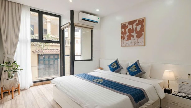 Quarto de hotel com cama, mesa de cabeceira, luminária, janela com cortinas e ar-condicionado fixado na parede.