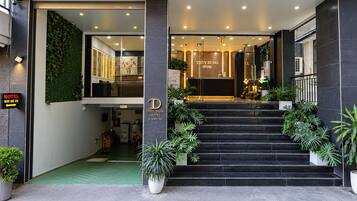 Entrada de hotel com balcão de recepção, escada que leva ao lobby e plantas em vasos.