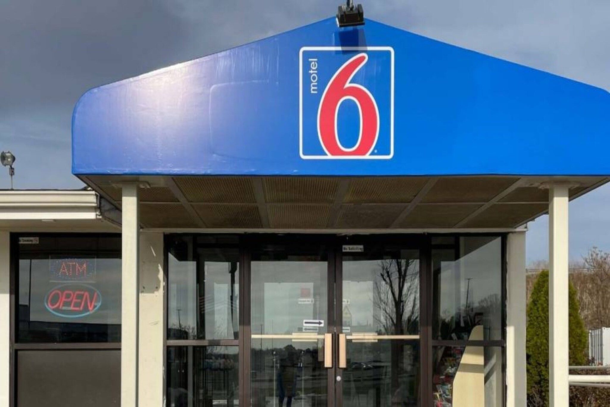 Une enseigne bleue de motel avec le chiffre 6, une entrée en verre et un panneau indiquant la présence d’un distributeur automatique de billets, ce qui signifie qu’il est ouvert.