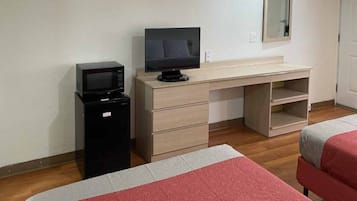 A hotel room with a bed, a desk with a television, a microwave, and a small refrigerator.