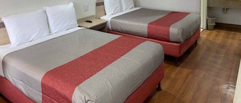 Dos camas con ropa de cama roja y gris, un suelo de madera y una mesita de noche con lámpara.