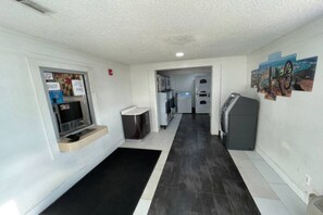 A narrow hallway with a black and white tiled floor, a small seating area with a bench, a refrigerator, and a washing machine.