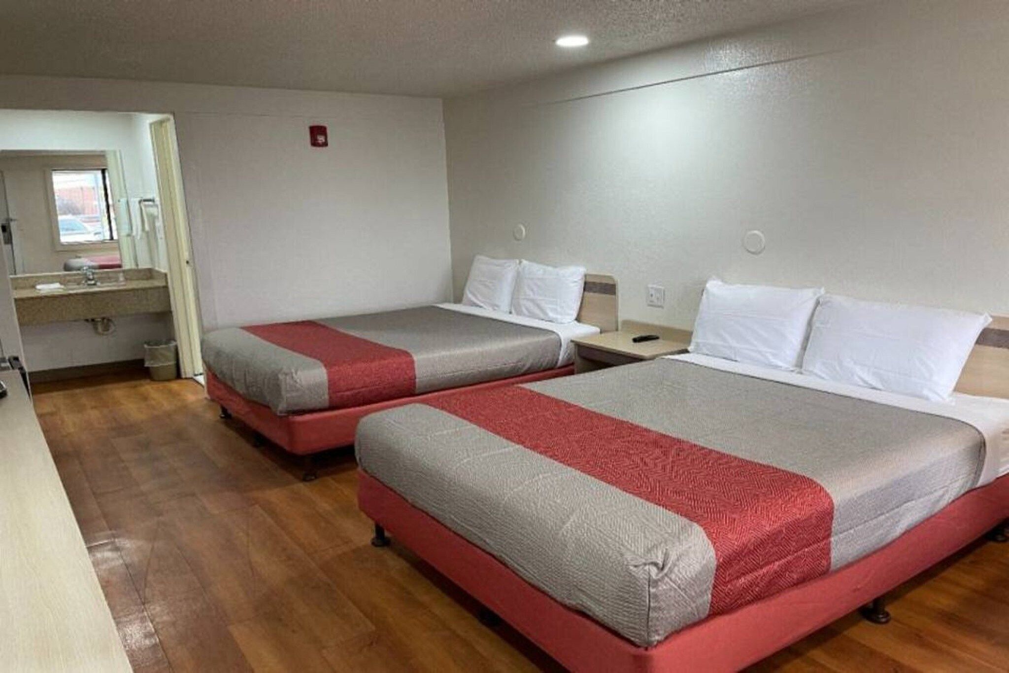 A hotel room with two beds, a small desk, and a window.