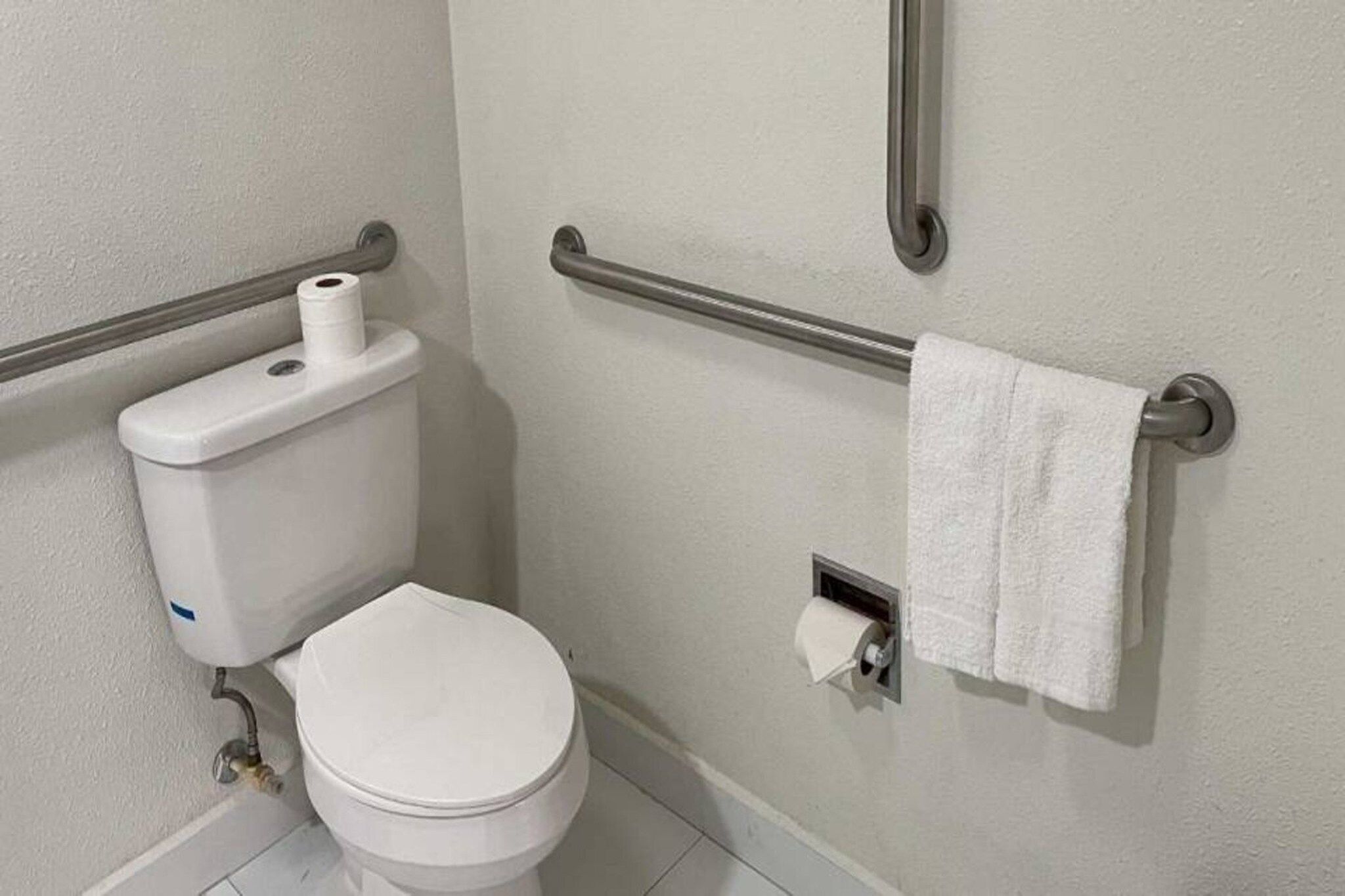 A standard white toilet with a paper towel holder and a towel rack on the wall.