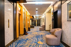 Un pasillo de hotel con alfombra estampada, una zona de estar y un mostrador de recepción.