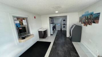 A narrow hallway with a black and white tiled floor, a small seating area with a bench, a refrigerator, and a washing machine.