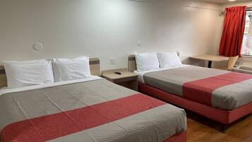 Una camera d'albergo con due letti, ognuno con cuscini bianchi e biancheria rossa e grigia. Nell'angolo, un tavolino e una sedia.
