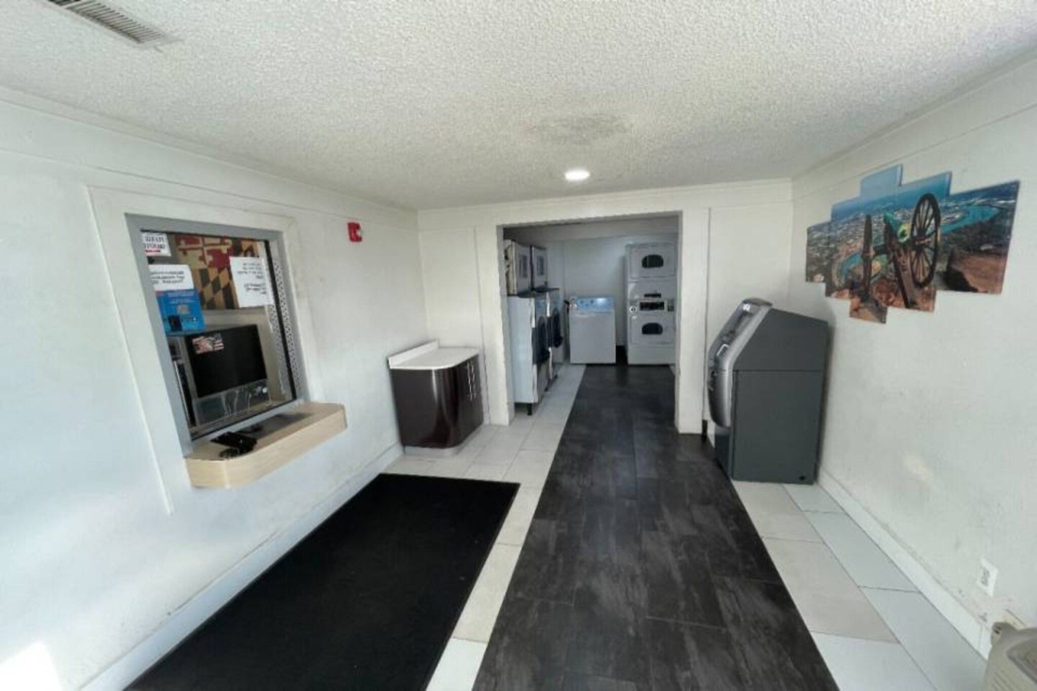 A narrow hallway with a black and white tiled floor, a small seating area with a bench, a refrigerator, and a washing machine.