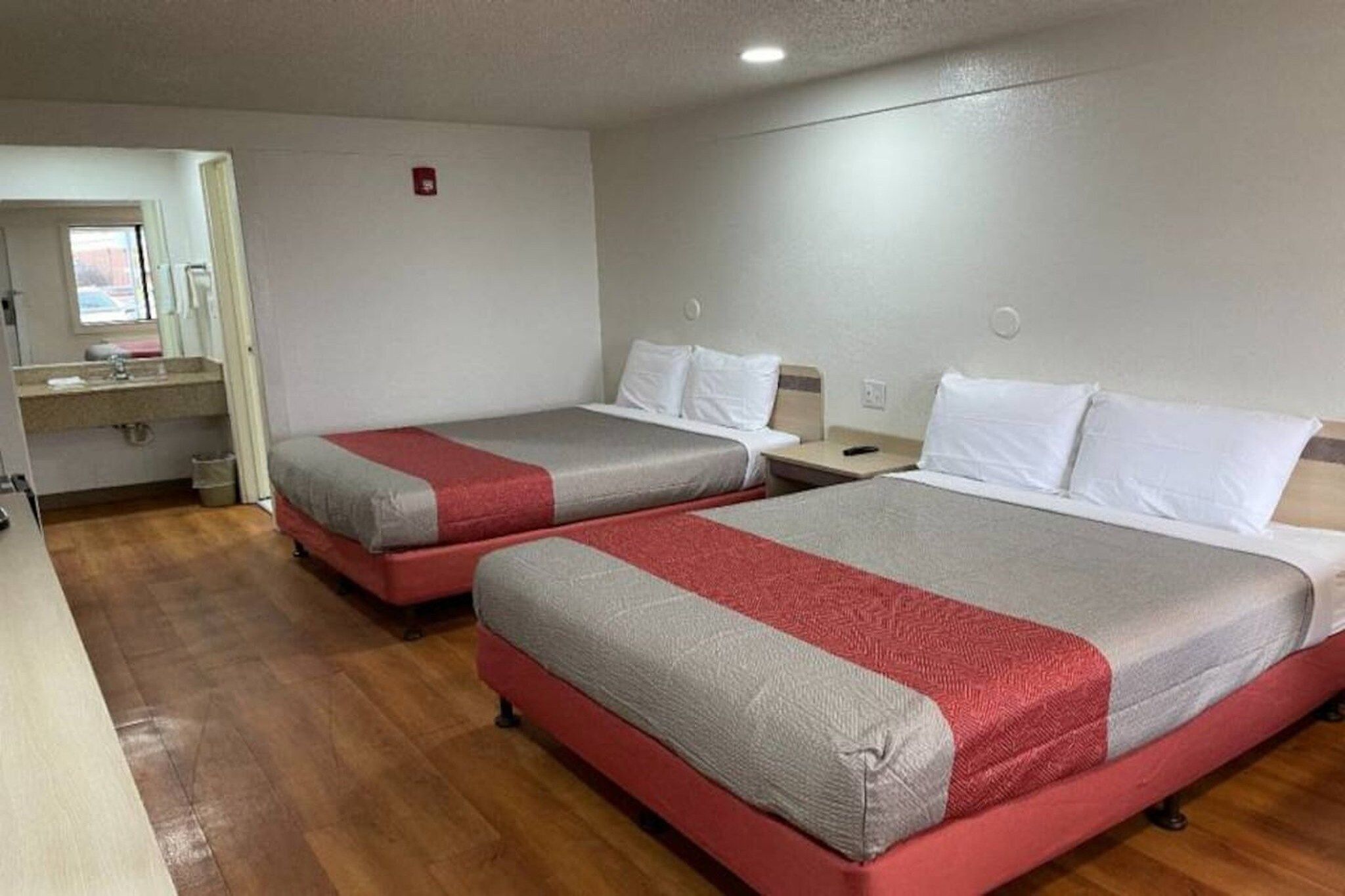 A hotel room with two beds, a small bathroom, and a window.